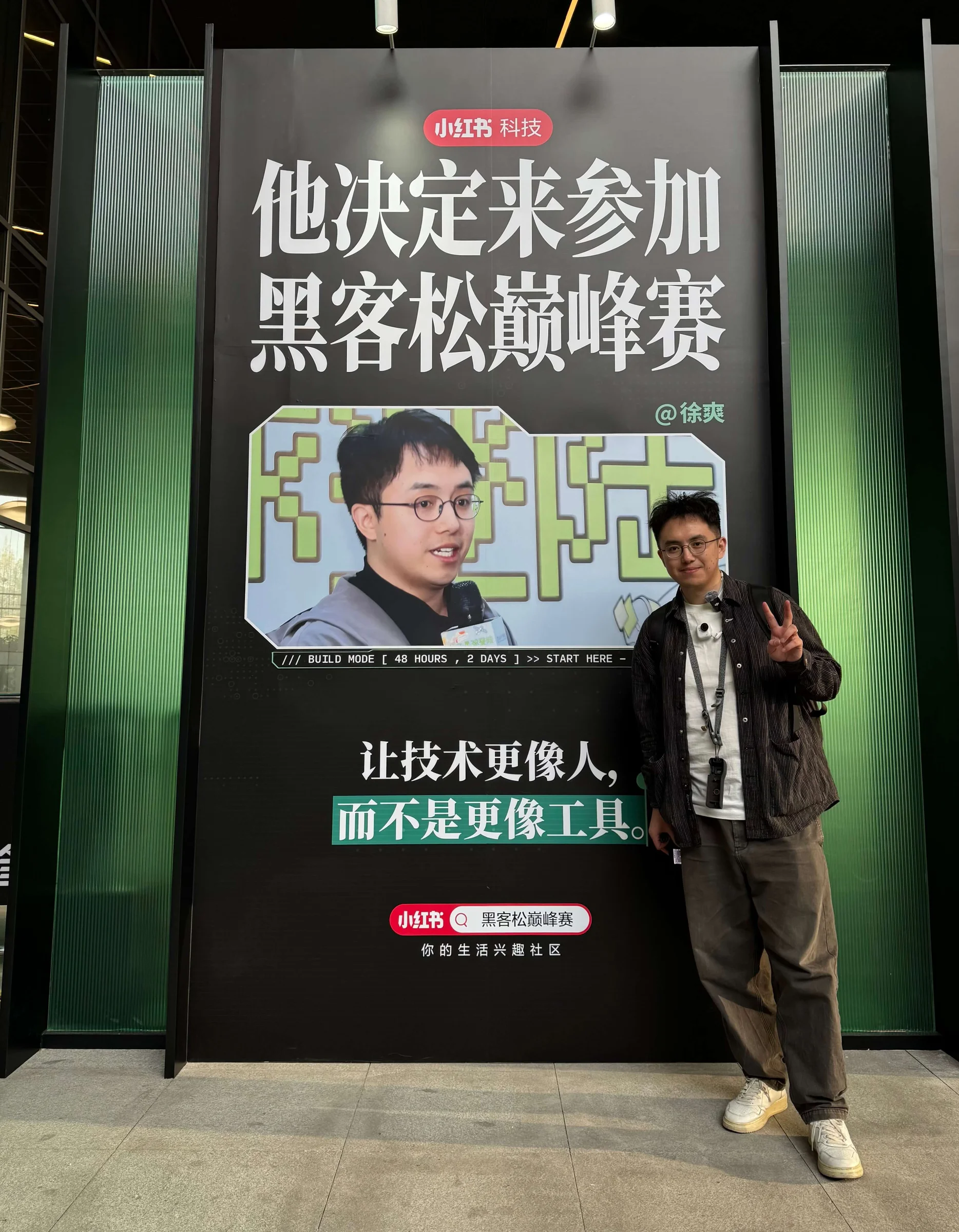 A梦站在黑客松巅峰赛现场的个人海报旁合影